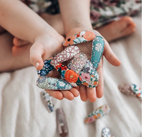A Collection of fabric covered hair clips held in the hands of a little girl - Raspberry Lane Baby and Kids 