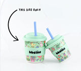 Two mint green cups with colorful designs and blue straws on a white background.