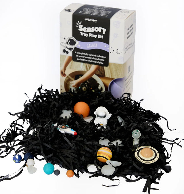 Sensory play kit with planets and stars on a black shredded paper base, featuring a box labeled 'Sensory Play Kit' in the background.